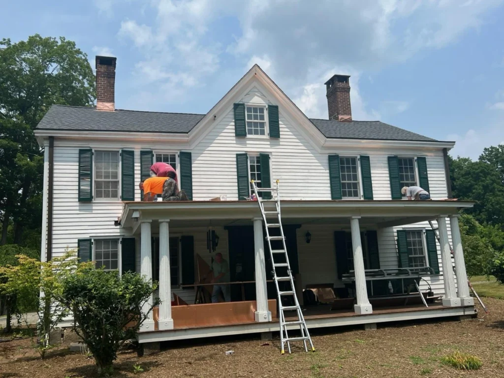 men working on a newly installed shingle roof on a house with white siding