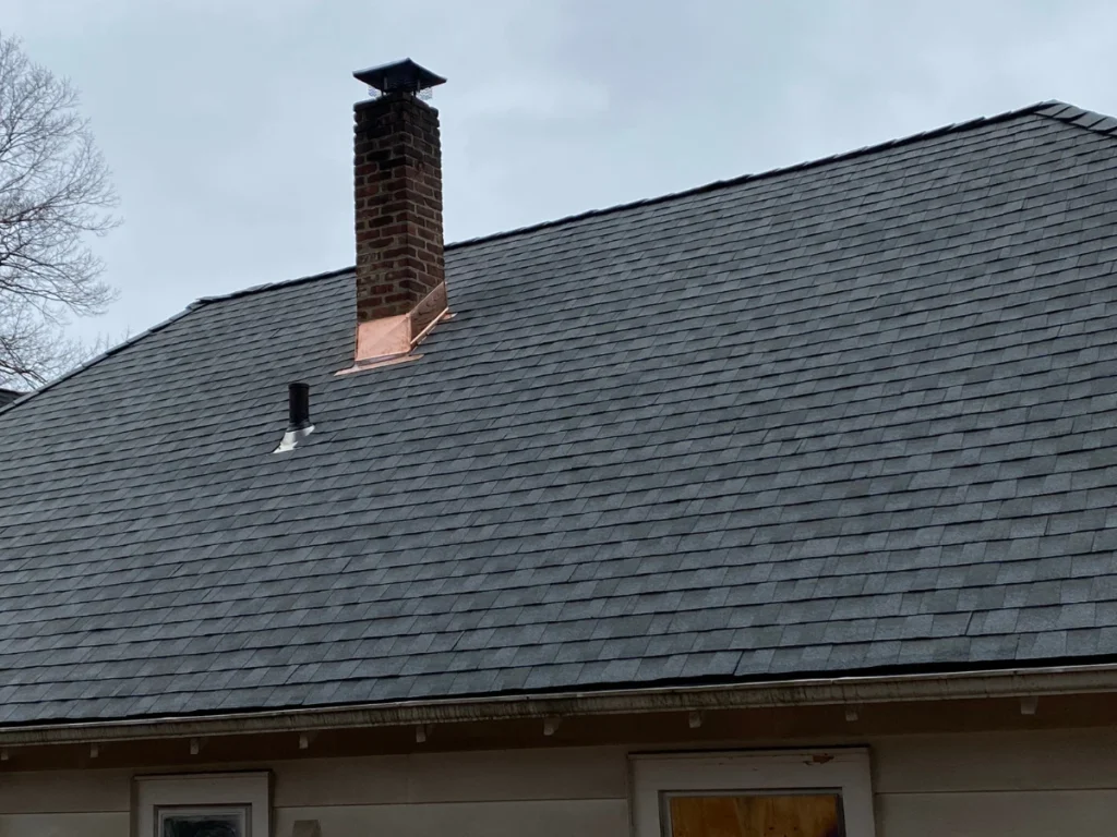 new grey roof shingles with copper flashing around chimney