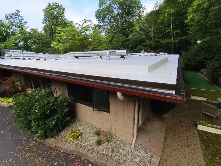 Side view of white flat roof with ductwork on tan brick building near Armonk