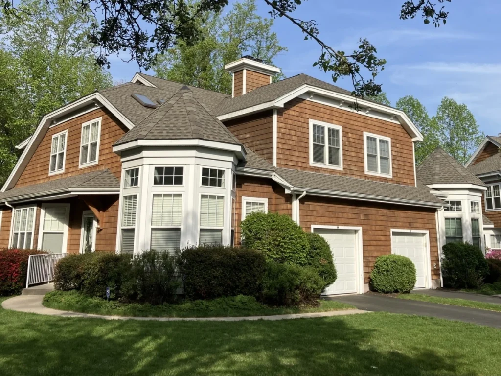 Two-story townhouse with brown wood siding and gray shingle roof, featuring bay windows.