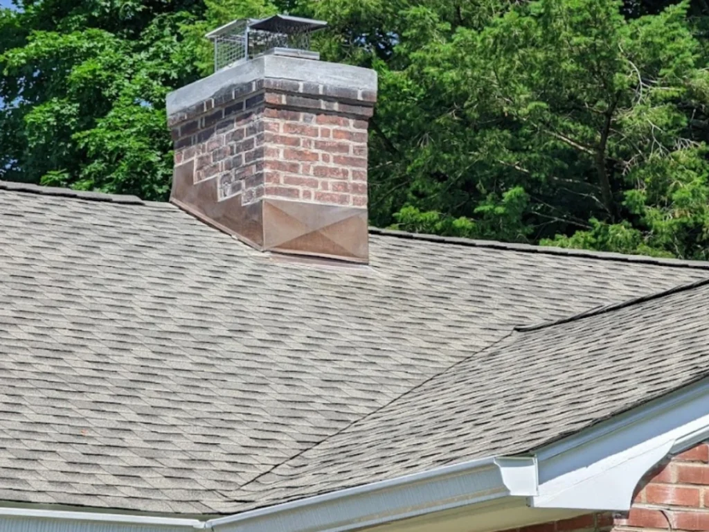 Close-up of a gray shingle roof with a brick chimney and copper flashing.
